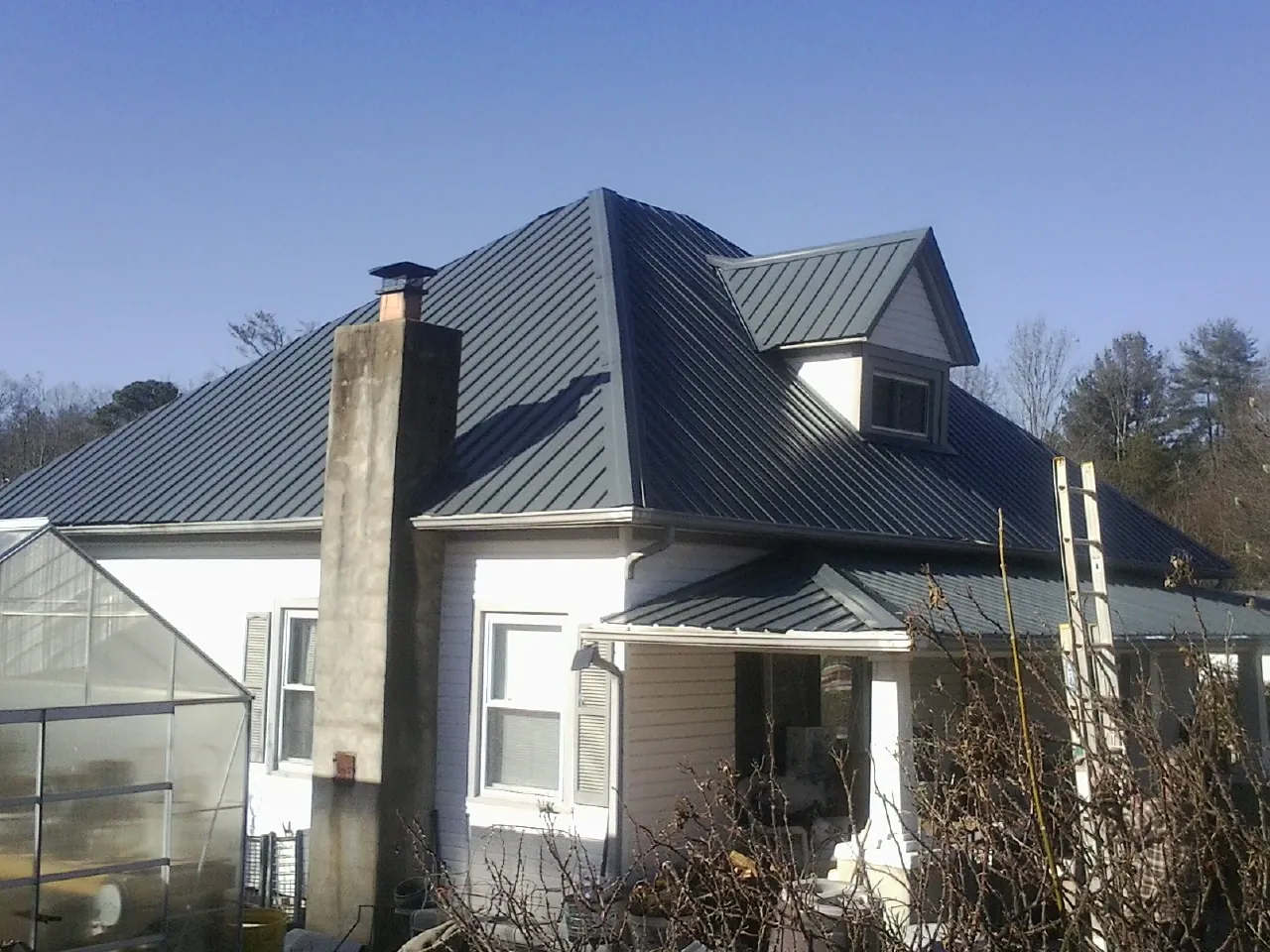 Dark blue standing seam metal roof on a white farmhouse with dormer — Slate & Tile Roof Repair by Roofing Brothers in Chittenango