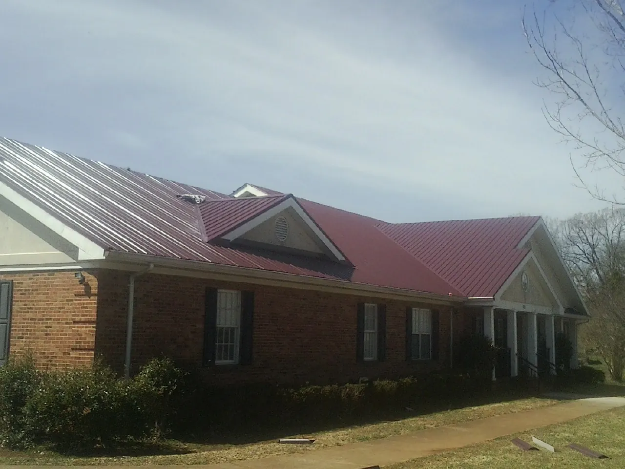 Red metal roof with gabled entries on a long brick building, from a Hail Damage Roof Repair job in Chittenango