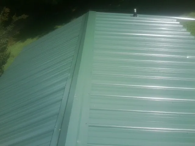 New green metal panels meeting at the ridge of a roof — Flat Roof Repair work by our crew in Chittenango