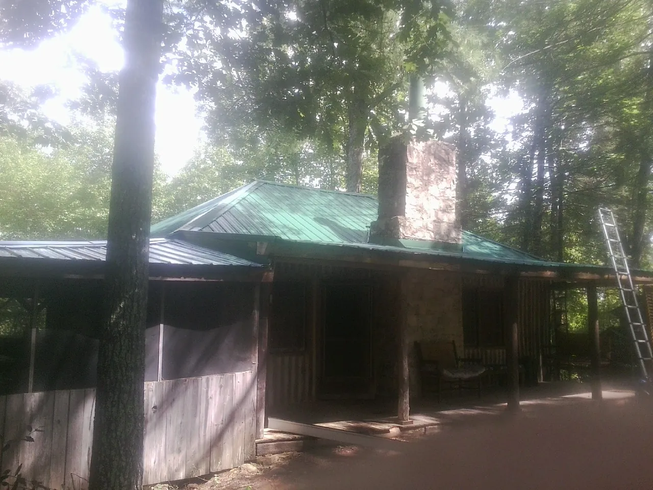 Green metal roof and stone chimney above a log cabin porch in Chittenango