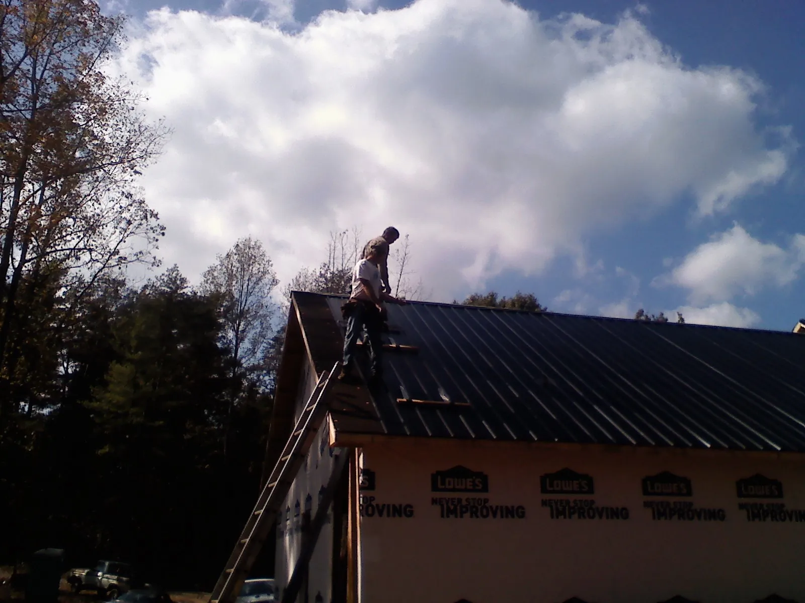 Roofer fastening dark metal panels high against a cloudy sky, from a Roof Inspection job in Chittenango