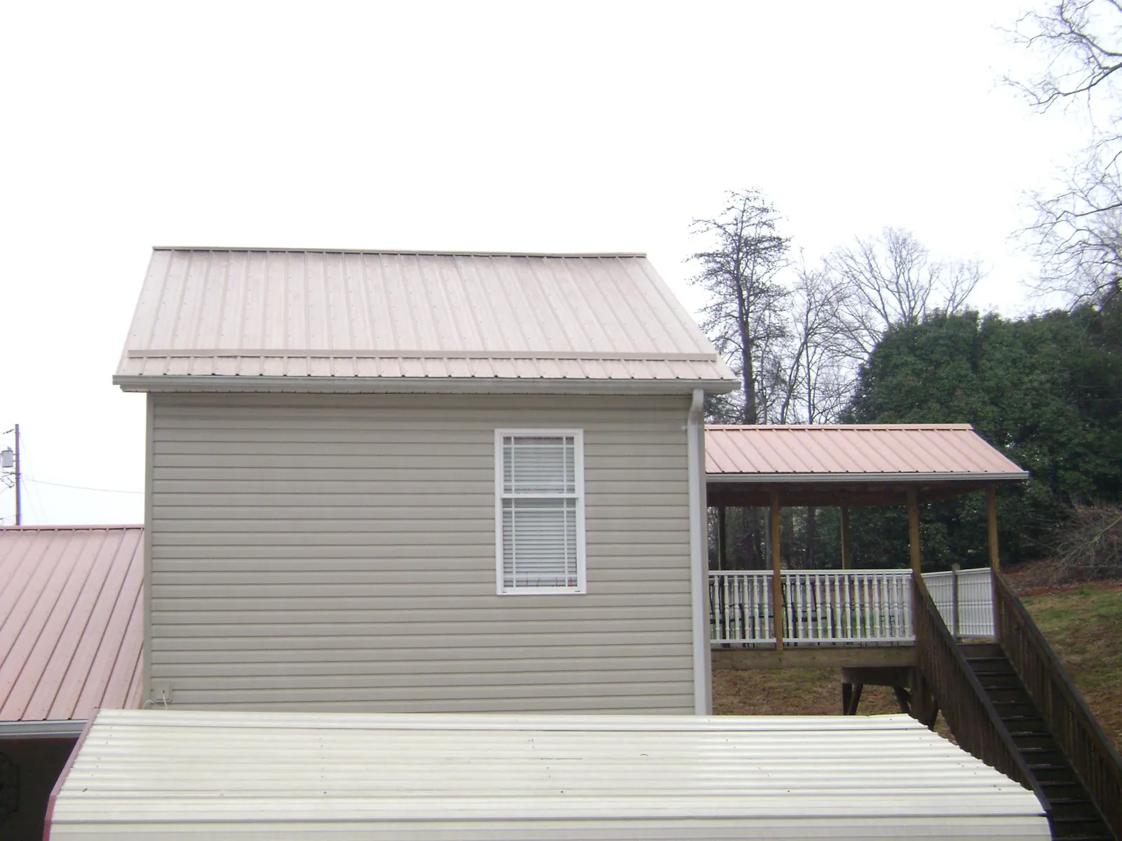 Tan metal roofs on a two story addition and attached porch, from a Roof Replacement job in Chittenango